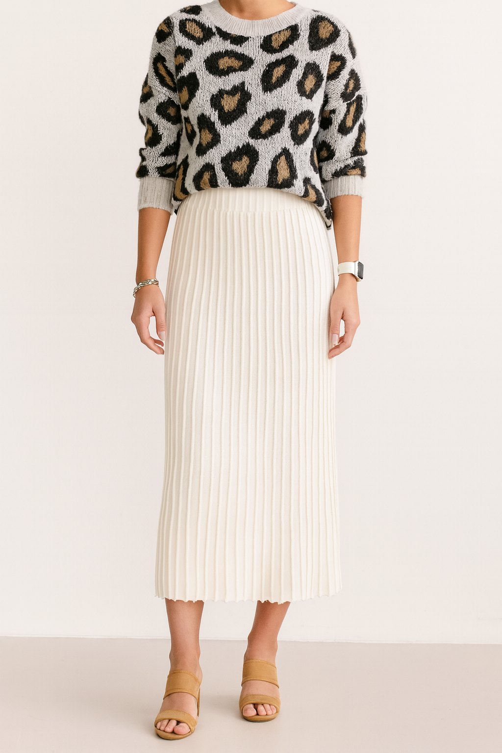Person wearing a leopard print sweater and white pleated skirt on a plain background