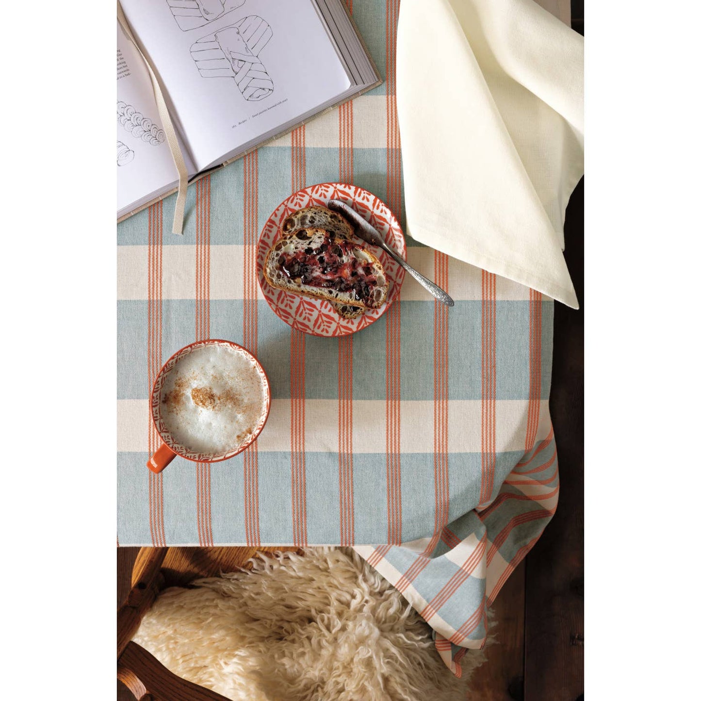 Table setting with a mug, plate, and book on a striped tablecloth.