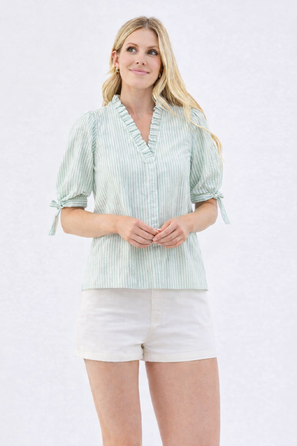 Woman wearing a light green striped blouse and white shorts on a white background